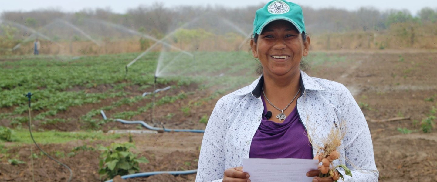 Una mujer en Bolivia con un campo de cultivo al fondo 