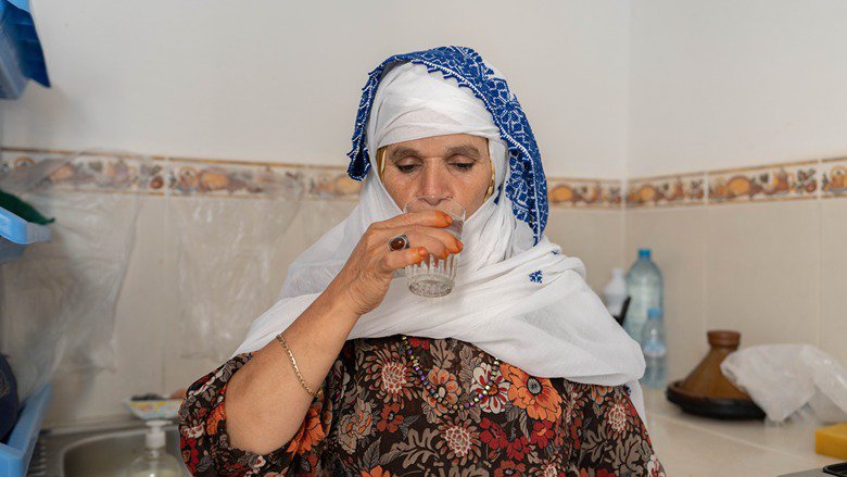 Beneficiary of household connection drinking clean water from the tap in her house
