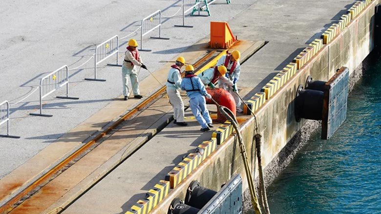 A group of port workers fasten ship mooring ropes to a bollard.