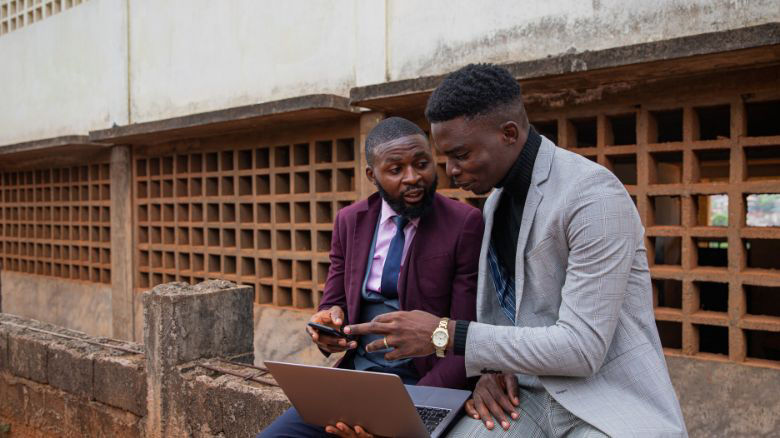 Two young Congolese men make use of a laptop and cellphone to conduct their digital business