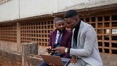 Two young Congolese men make use of a laptop and cellphone to conduct their digital business