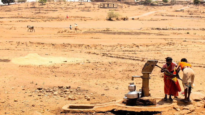 Tribal woman pumping water from hand pump, India
