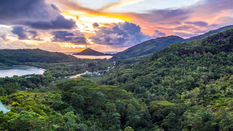 Mahe Island coast drone sunset landscape with dramatic pink sky, clouds, lush tropical forest and small islands around