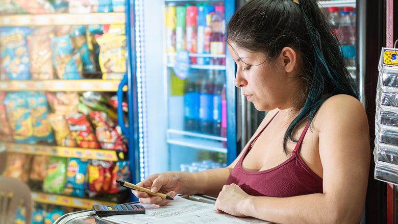 latina woman concentrating while calculating the number of sales in a notebook of her grocery store
