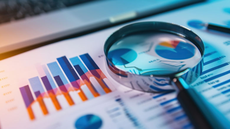 A magnifying glass glancing over a document containing infographics, stats, and geometrical pies.