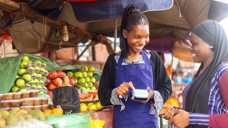 Young African female fruit merchant  attending to buying client while holding an card reader