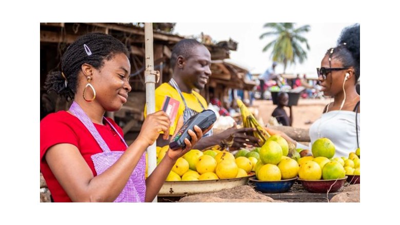 An African woman uses a card reader to facilitate digital transactions for her fruits business at the local marketplace