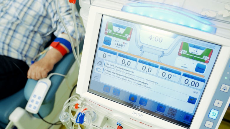 Close-up of the screen of a dialysis machine being prepared for a patient sitting nearby