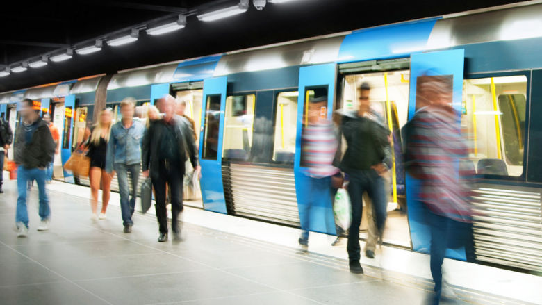 Commuters entering and exiting a blue metro train at a busy underground subway station