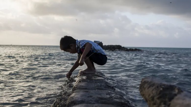 A boy plays on a flooded sea wall in Bikenibeu village, South Tarawa island of Kiribati. Photo: Conor Ashleigh/World Bank