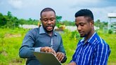 Young Cameroonian men standing on a farmland and reading a business plan on a laptop to be executed on the farmland