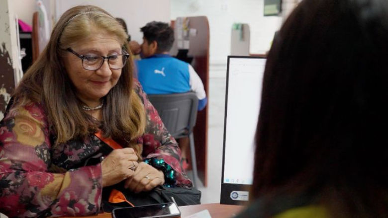 A Latin American woman discusses receiving her benefits in her mobile phone with a government official