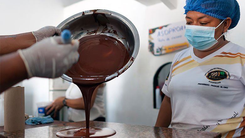 Chocolate cayendo en molde mientras trabajadora lo observa