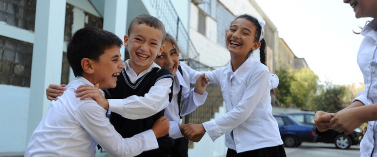 Group of school children laughing and playing together in a courtyard, wearing uniforms and enjoying recess.