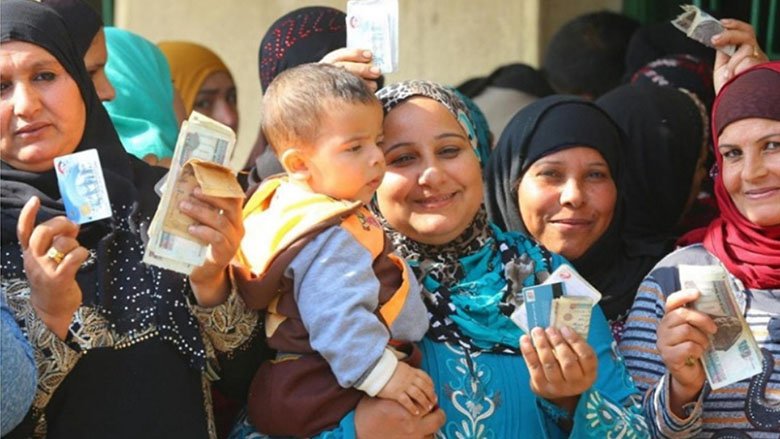 Several smiling Egyptian women show their Takaful and Karama debit cards and hold the cash