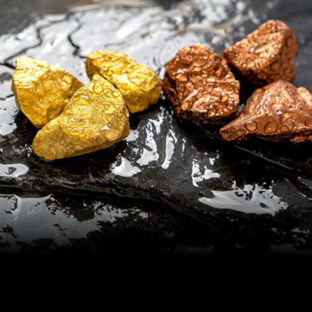 Close‑up of wet gold and copper mineral rocks resting on a dark stone surface.