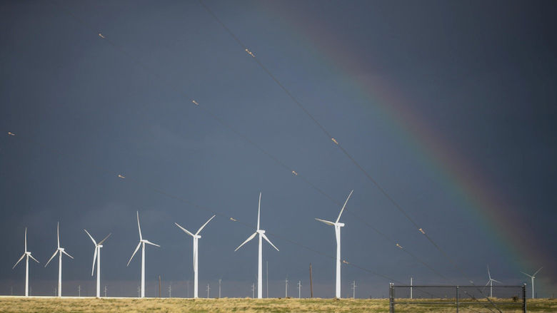 White windmills in an empty field with a gray sky and a rainbow in the upper right corner