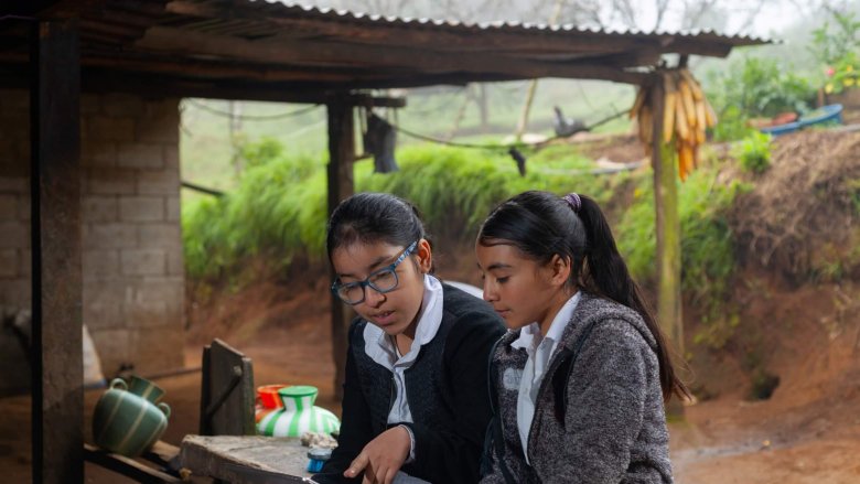 Two young girls in a village in Ecuador use a tablet to complete their after school activities