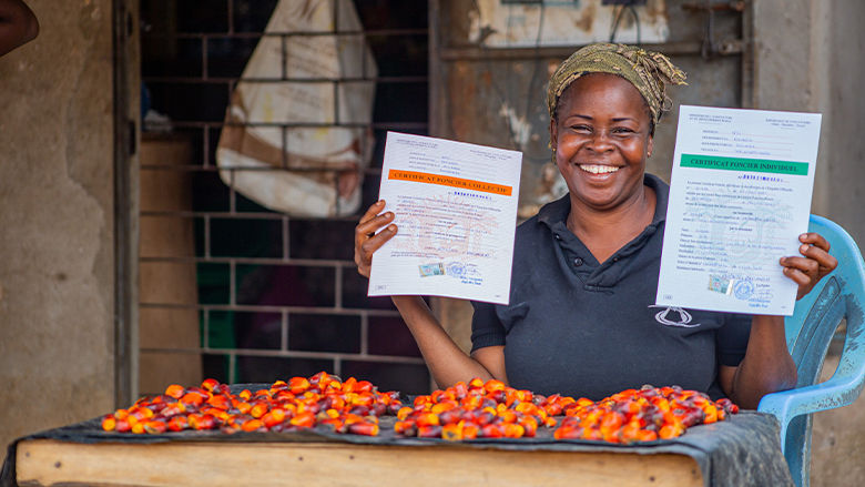 photo of an Ivorian female entrepreneur holding copies of land rights in each hand. 