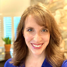 Female with red hair smiling and wearing a blue top