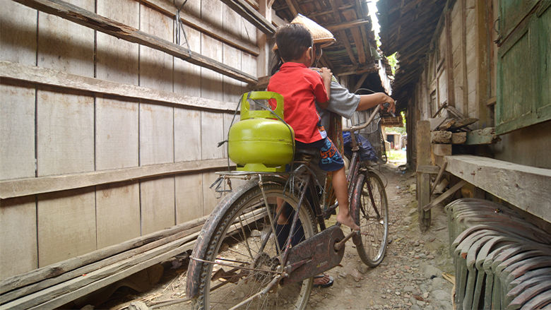 A resident transports an LPG cylinder through a rural Indonesian community, illustrating the role of clean cooking fuels in e