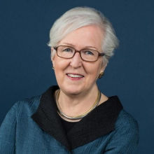 Female with white pixy hair, wearing blue blouse and eyeglasses 