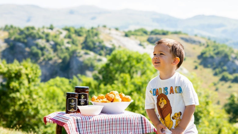 Young child stands next to a table with a checkered cover, with honey and bread on top.