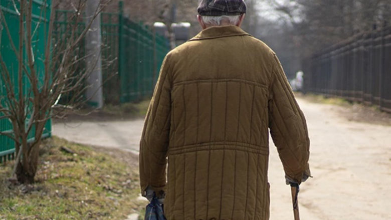 old man walking on the street with a stick, view from his back