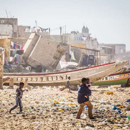 Children playing on a beach full of debris, nearby boats and with houses destroyed by rising waters in the background.