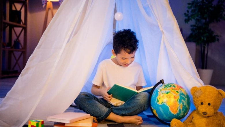  young boy sitting in a homemade tent and reading an interesting book in his room. Photo credit: Deagreez / AdobeStock