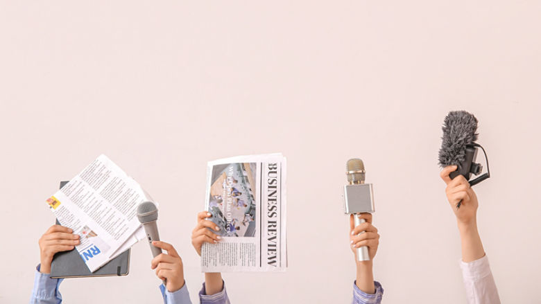 Female hands with newspapers and microphones on light background