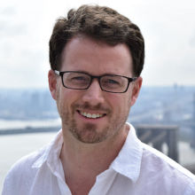 White male smiling, wearing eyeglasses and white blouse