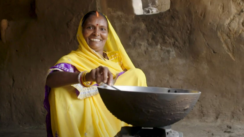 An image of a woman in a yellow sari cooking.