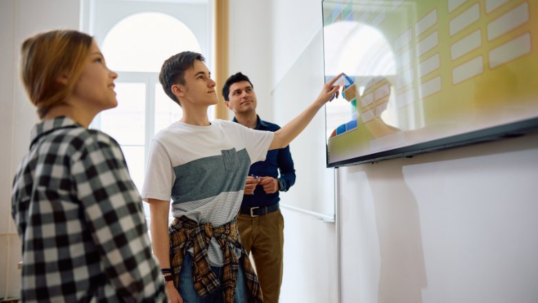 Two male and one female teenagers use a digital board to solve problems in class