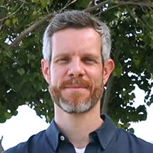 Male with white hair and brown beard wearing a dark blue blouse