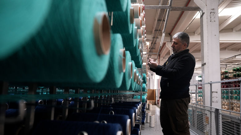 A man inspecting spools of turquoise and blue carpet thread at a factory in Gaziantep, Türkiye 