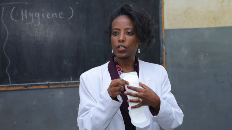Teacher holding a sanitary pad and explaining to students how to use it