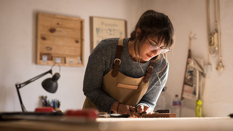Young business woman handcrafting a piece of timber and designing new house furniture in her workshop.