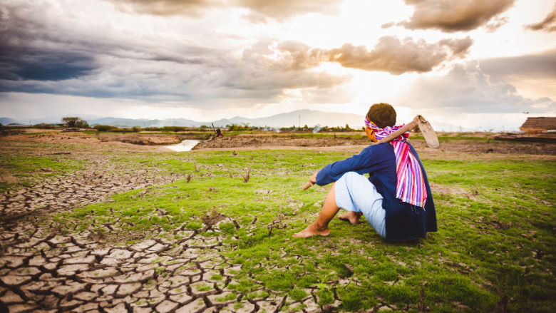 A female farmer sits on a patch of greenery amidst a dry land