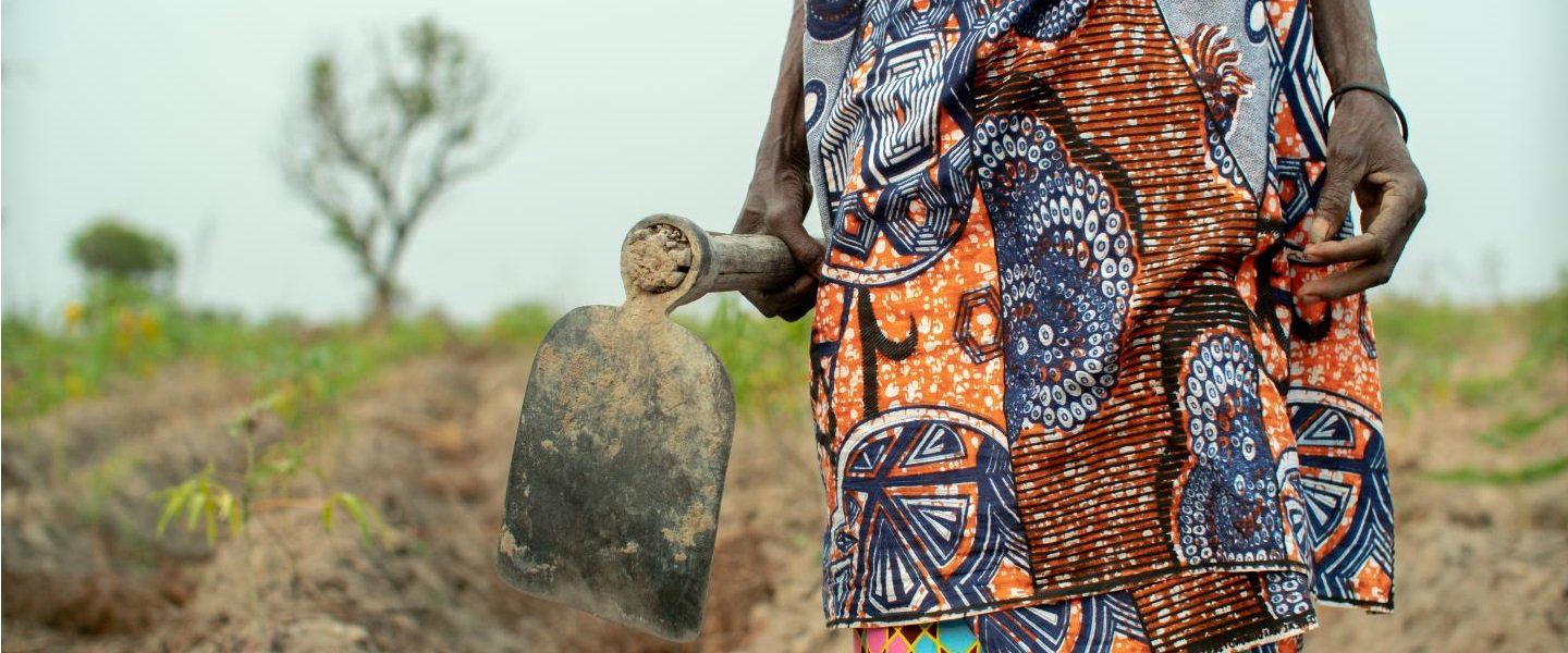 A woman farmer in Angola carrying a hoe in a field