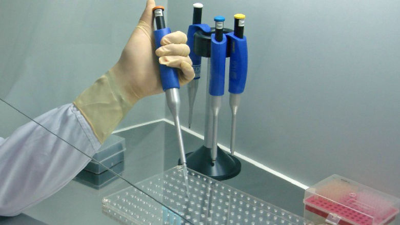 A person with a lab coat on uses a dropper to put liquid into a test tube in a laboratory. 