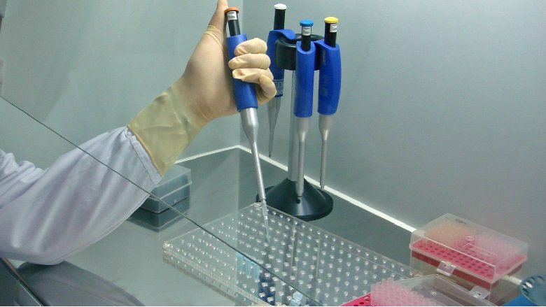 A person with a lab coat on uses a dropper to put liquid into a test tube in a laboratory. 