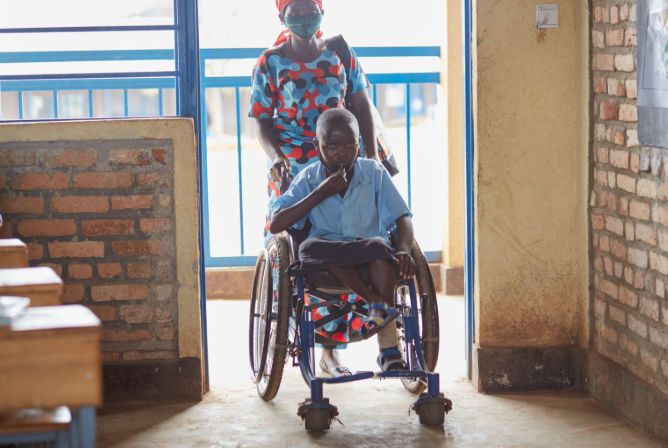 A mother in Rwanda pushes her daughter with a disability into her classroom.