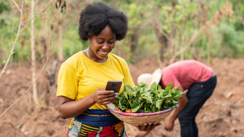 Female farmer holding basket of agricultural products while checking her phone