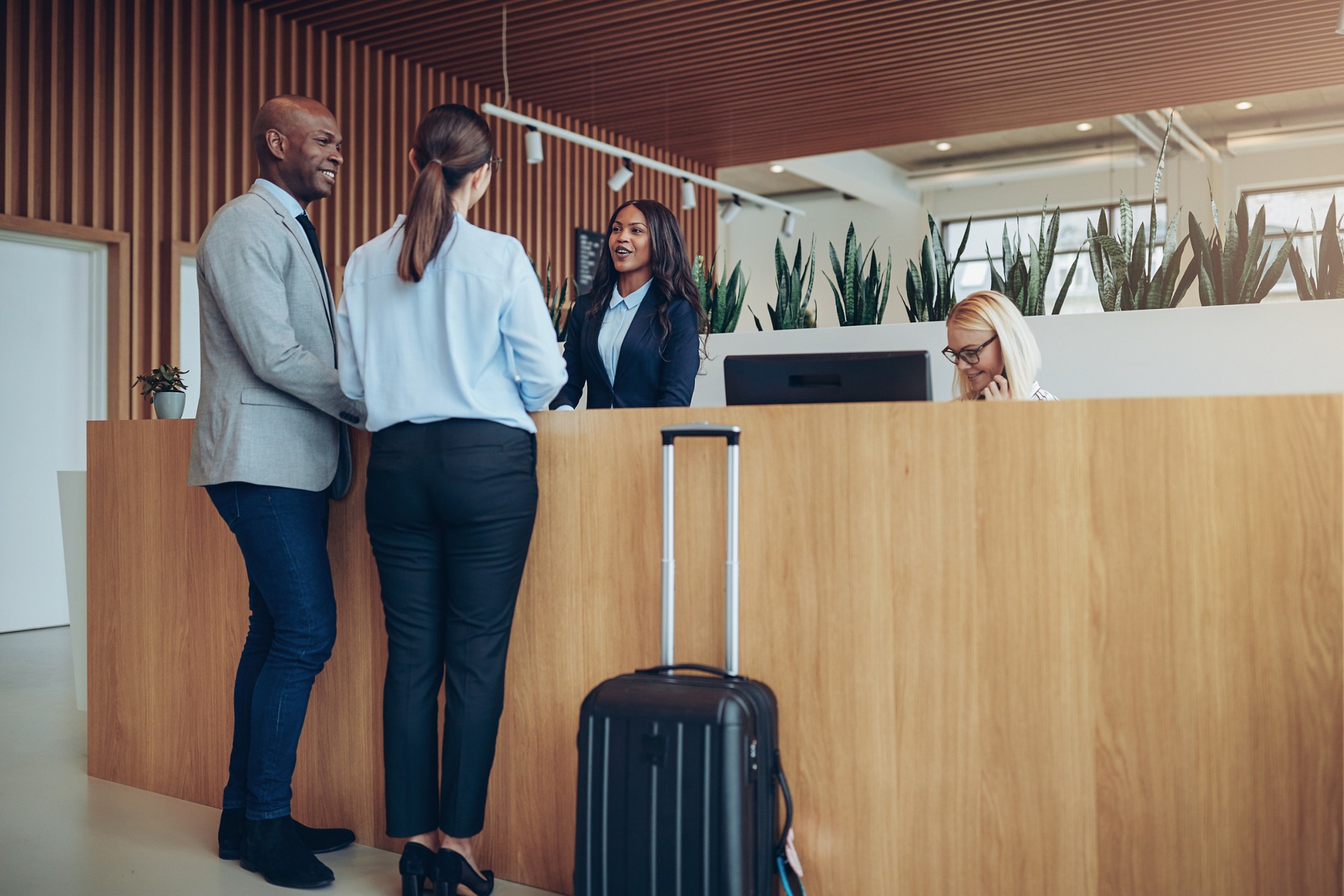 Two smiling guests talking with a concierge while checking in together at the reception counter of a hotel