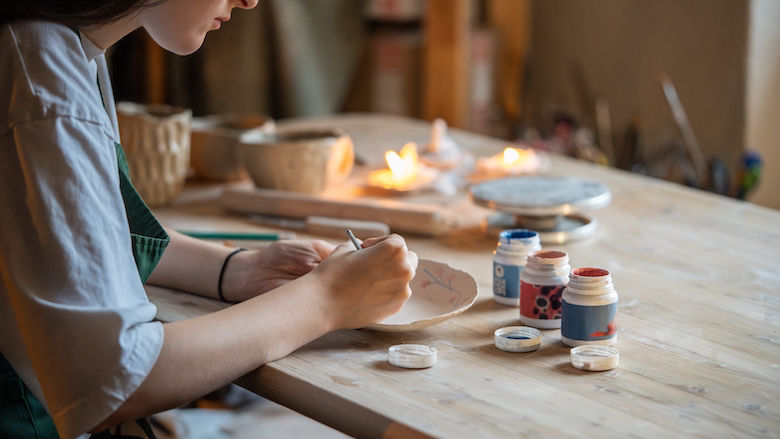 MENA: Decorating pottery. Woman ceramist holding paintbrush and drawing cute ornament on clay plate. Creative classes of work