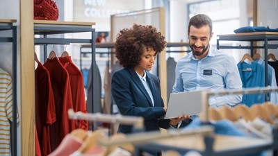 Clothing Store: Businesswoman Uses Laptop Computer, Talks to Visual Merchandising Specialist, Collaborate To Create Stylish Collection. Small Business Fashion Shop Sales Manager Talks to Designer.