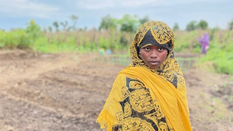 Sudanese refugee woman standing in front of farmland