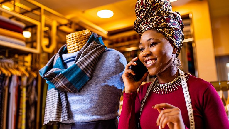 tanzanian woman with snake print turban over hear working in fabrics shop calling to client by smartphone